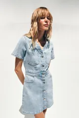 Vestido corto de denim azul, con cuello solapa, escote en V, manga corta, bolsillos delanteros y cierre frontal con botones metálicos.
