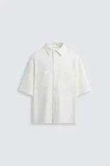 Sobrecamisa blanca de manga corta con cuello solapa, bolsillos de plastrón en el pecho y cierre frontal con botones a presión.