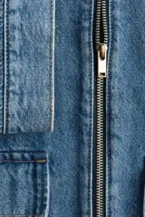 Campera de denim azul de algodón rígido con cuello, cierre delantero y canesú en la espalda. Modelo con puños abotonados, bolsillos delanteros con solapa y bolsillo interior de parche en el pecho. Trabillas ajustables con botones en la parte posterior del bajo.