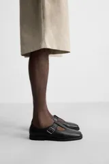 Zapato tipo Mary Jane de cuero negro con hebilla lateral, horma redonda y suela con ligero tacón.