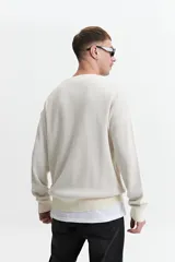 Buzo de punto color crudo, de corte oversize, con cuello redondo y puños.