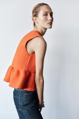 Top tejido de punto color naranja, de cuello redondo y sin mangas. Tiene corte ajustado en el torso y peplum en la cintura.