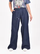 Pantalón de jean azul oscuro de tiro alto, corte ancho y pierna acampanada. Presenta pliegues frontales y un lazo de tela a tono para ajustar en la cintura.