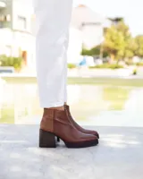 Botines de cuero marrón, hechos a mano en Uruguay, con plataforma delantera y taco ancho y alto de color negro. Presentan un detalle de textura de piel de reptil en la parte superior del talón y cierre lateral con cremallera.