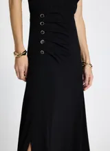 Vestido midi negro de punto, con un solo hombro, detalle de nudo en el hombro y botones metálicos decorativos en el lateral.