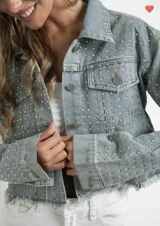 Campera de jean celeste con cuello clásico, cierre frontal con botones metálicos y dos bolsillos con solapa en el pecho. Está decorada con strass plateados en toda la superficie y tiene terminaciones desflecadas.