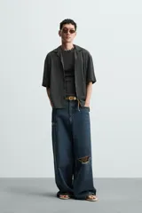 Camisa de manga corta con cuello bowling y calce relajado. Presenta un tejido con textura estructurada y efecto lavado, con cierre frontal de botones al tono.