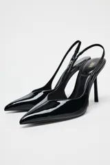 Zapato destalonado negro acharolado con tacón fino y punta. Tiene una tira trasera con elástico.