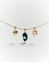 Dije charm colgante de oro con forma de trébol de cuatro hojas, llave y piedra verde. El dije se engancha a una cadena de oro con pequeñas cuentas.