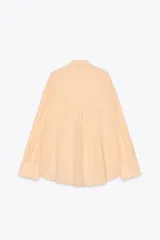 Camisa color durazno confeccionada en algodón, de corte amplio, con cuello solapa, manga larga con puños abotonados, hombros caídos, bolsillo de parche en el pecho, pinzas en la espalda y cierre frontal con botones.