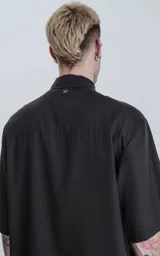 Camisa de manga corta, color negro liso, con cuello camisero y cierre frontal de botones. Corte holgado.