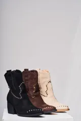 Bota corta de gamuza color beige con taco cuadrado y punta fina. Presenta una correa con tachas pequeñas y una argolla metálica decorativa alrededor del tobillo. Cuenta con cierre lateral.