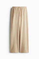 Pantalón de punto color beige, de corte holgado con piernas amplias, tiro alto, cintura elástica y cordón para ajustar.