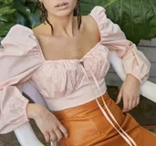 Top color rosa claro, confeccionado en tela tipo camisa, con mangas abullonadas, escote cuadrado con lazo ajustable y cierre lateral invisible.