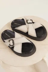 Sandalias planas color beige con tiras cruzadas y hebilla decorativa.