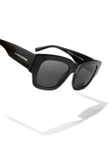 Gafas de sol unisex Hawkers X Augusto Fernandez, de acetato negro con lentes polarizadas negras y logo de la marca en la patilla.
