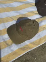 Gorra de béisbol color marrón con bordado frontal de la palabra "MILO" en color dorado.
