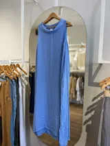 Vestido largo sin mangas color azul claro, confeccionado en lino, con cuello tipo buche o drapeado. Presenta un calce holgado y bolsillos laterales.