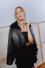 Campera bomber negra de cuero con cuello de piel sintética, forro interior y detalles de pasamanería en cuero marrón gastado.