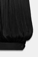 Mono de mujer color marrón oscuro, con escote redondo y tirantes finos. El tejido es satinado y plisado verticalmente. El pantalón es estilo bombacho con bajo abullonado ajustado con botón.