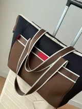 Bolso tipo tote de neopreno color negro y marrón, con cierre superior, bolsillo frontal marrón con logo rojo, bolsillo interno y externo con cierre, doble asa de mano marrón con detalles blancos y opción de correa larga.