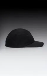 Gorra negra de cinco paneles con visera plana y un pequeño parche cuadrado blanco en el frente con un logo bordado en forma de tijeras cruzadas.
