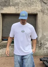 Remera blanca de algodón con corte boxy y parche bordado con la palabra "Brokers" en óvalo azul y verde.