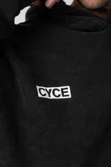 Buzo canguro negro de frisa rústica con corte oversize y capucha. Presenta un pequeño logo blanco en el pecho y un bolsillo tipo canguro.