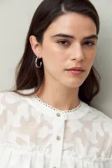 Camisa blanca de encaje bordado con diseño semitransparente, silueta fluida y mangas largas. Se destaca por los volados en el frente y hombros.