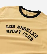 Remera de manga corta estilo ringer, color amarillo claro con ribetes negros en cuello y mangas. Presenta un estampado central en negro con el texto "Los Angeles Sport Club".