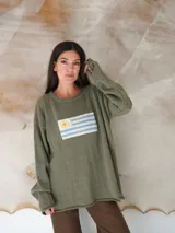Sweater beige de hilo de algodón con cuello redondo y manga larga. Estampado con la bandera de Uruguay en el frente.