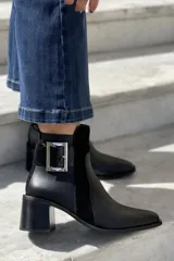 Bota de cuero negro con cierre lateral interno y hebilla decorativa en el costado exterior.