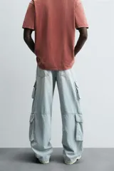 Pantalón de denim color beige, corte relaxed fit, con bolsillos laterales tipo cargo con solapa y cierre de botón. Cierre frontal con botón y cremallera.