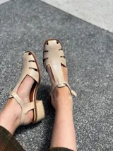 Sandalias nude de cuero con diseño calado y tira con hebilla al tobillo.