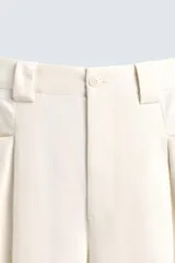 Pantalón color crema de corte ancho, con pliegues frontales, bolsillos laterales y traseros.