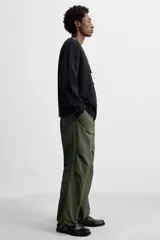 Pantalón verde militar de corte relaxed fit confeccionado en tejido técnico ligero. Cuenta con cintura elástica ajustable con cordón interior, bolsillos frontales y traseros con solapa, pliegues en las rodillas y bajo ajustable con elástico.