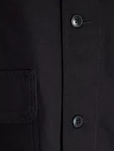 Campera negra corta de algodón, con cuello clásico, cierre con botones, puños abotonados y bolsillos frontales.