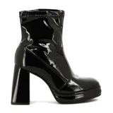 Bota corta de charol color crema, estilo botín, con caña elástica y puntera cuadrada. Presenta una plataforma delantera y un taco ancho y alto.