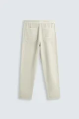 Pantalón color arena de corte recto, confeccionado en tejido de algodón y lino. Cuenta con cintura elástica ajustable con cordón, bolsillos delanteros y traseros de parche.