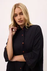 Vestido camisero a rayas verticales de colores pastel, con cuello camisero, cierre frontal con botones y mangas largas.