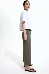 Pantalón cigarette tobillero color verde oliva, con cintura estándar, cierre y pretina prolongada con corchete oculto. Piernas ajustadas con abertura corta en los bajos, bolsillos al bies y bolsillo de atrás decorativo. Pliegues adelante y atrás.