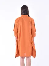 Vestido camisero color naranja de corte holgado, con cuello camisero, mangas cortas tipo kimono y cierre frontal con botones.