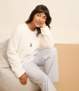 Pijama largo de sherpa color blanco, compuesto por un buzo de cuello redondo y mangas largas con estampa de una carita sonriente y un pantalón con estampa de lunares.