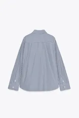 Camisa blanca de popelina de algodón, con cuello solapa y mangas largas con puños abotonados.