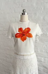Remera blanca de algodón con estampado de flor naranja.