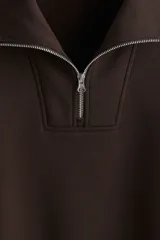 Buzo de tejido pesado color marrón oscuro, con interior cepillado suave. Presenta cuello elevado, medio cierre metálico y hombros caídos. Puños y bajo en punto acanalado.