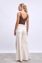 Pantalón de denim color crudo, corte ancho y tiro alto, con grandes calados florales bordados en contraste a lo largo de ambas piernas.