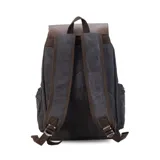 Mochila negra de tela canvas con detalles en símil cuero marrón, cierre superior marinero, bolsillos internos y externos con cierre metálico, asas rígidas y correas ajustables.