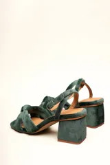 Sandalia de terciopelo verde con taco cuadrado de 7 cm, punta cuadrada y tiras anchas anudadas en el empeine. Cuenta con una tira fina ajustable al tobillo con hebilla dorada.