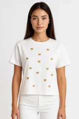 Remera blanca de algodón con cuello redondo y estampado de corazones dorados.